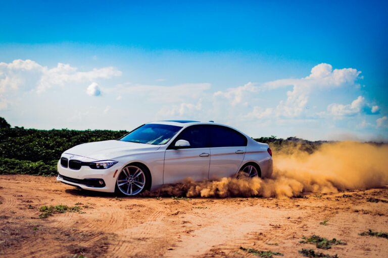 White luxury car drifting on a dirt road, creating a dramatic dust cloud under a blue sky.